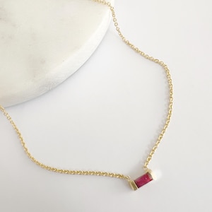 Pode incluir: Um delicado colar de corrente de ouro com um pequeno pingente retangular de pedra vermelha.