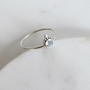 May include: A silver ring with a light blue gemstone and a delicate beaded design.