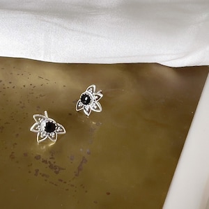 Puede incluir: Un par de pendientes de plata con detalles de piedras preciosas negras en forma de flor.