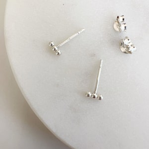 May include: A pair of silver stud earrings with three small balls on each earring.