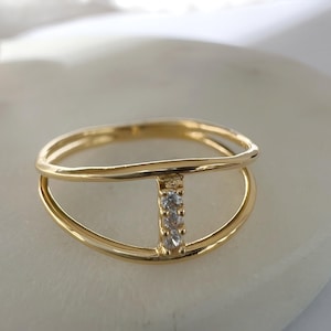 May include: A gold ring with a delicate, open design featuring two intertwined bands and a vertical row of three small, clear cubic zirconia stones.