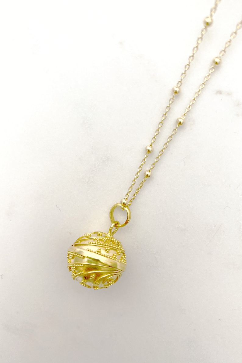 May include: A gold necklace with a delicate chain and a round, ornate pendant. The pendant has a textured, swirling design.