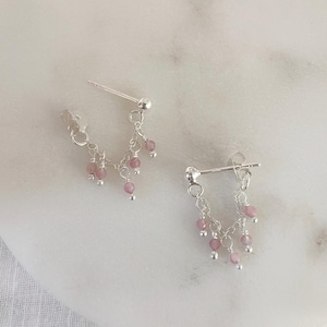 May include: A pair of silver earrings with a delicate chain and pink beads dangling from each earring.