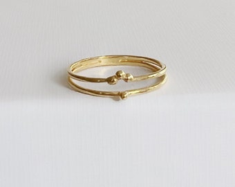 May include: A gold-colored ring with three bands. The middle band features three small, round embellishments. The ring is set against a white background, highlighting its simple yet elegant design. The ring appears to be made of metal.