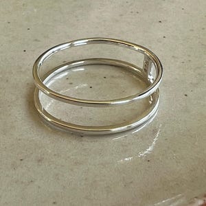 Puede incluir: Un anillo de plata de doble banda. El anillo está hecho de dos bandas de plata que están apiladas una encima de la otra. El anillo es simple y elegante.