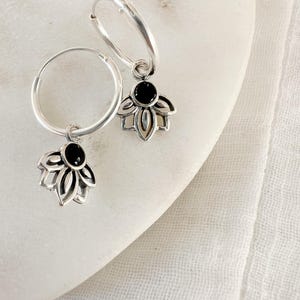 Peut inclure: Une paire de boucles d'oreilles créoles en argent avec un charme en forme de fleur de lotus en pierre noire suspendu à chaque créole.