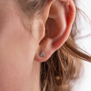 Puede incluir: Primer plano de una oreja con un pequeño pendiente triangular de plata.