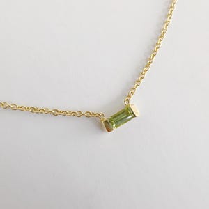 Peut inclure: Un collier délicat en chaîne dorée avec un petit pendentif en pierre précieuse verte rectangulaire.