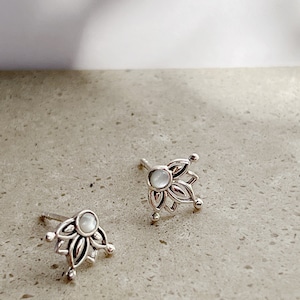 May include: A pair of silver earrings with a white mother of pearl centre and a delicate floral design.