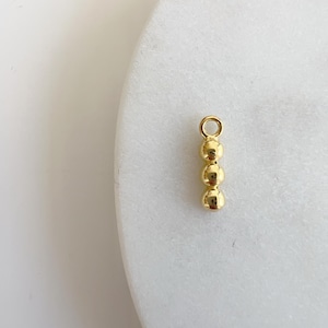 May include: Gold charm with four round beads. The charm has a loop at the top for attaching to a necklace or bracelet.
