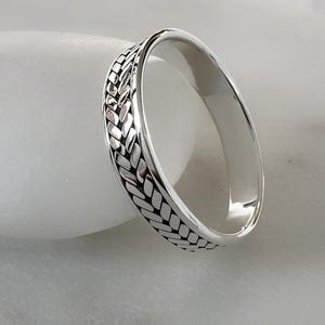 Puede incluir: Un anillo de banda de plata con un diseño trenzado.