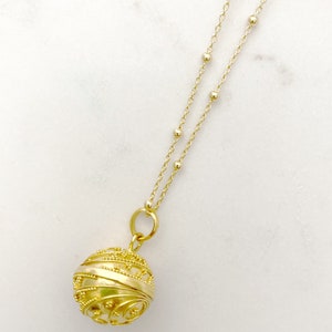 May include: A gold necklace with a delicate chain and a round, ornate pendant. The pendant has a detailed, intricate design and appears to be hollow.