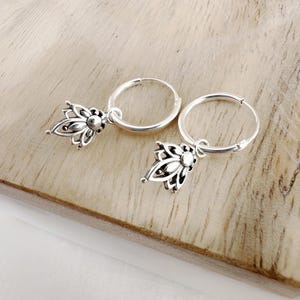 Puede incluir: Un par de pendientes de aro de plata con un colgante de flor. Los pendientes son simples y elegantes, perfectos para el uso diario.