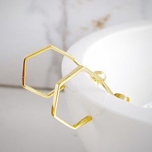 May include: A pair of gold hexagonal hoop earrings. The earrings are simple and modern in design.