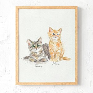 May include: Watercolour painting of two cats in a wooden frame. One cat is grey and brown, lying down, with green eyes. The other is orange, sitting up, with blue eyes. The names "Tommy" and "Millie" are written below the cats.
