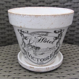 Könnte beinhalten: Weißer Blumentopf aus Keramik mit einem schwarz-weißen Design mit dem Text "L'Hotel Victoire Paris".