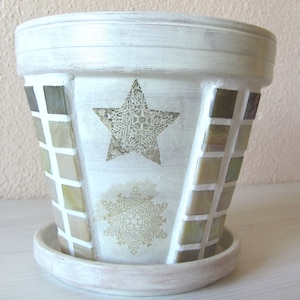Könnte beinhalten: Weißer Keramiktopf mit Mosaikdesign mit einem goldenen Stern und einer Schneeflocke. Der Topf hat einen weißen Sockel.