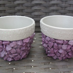 Peut inclure: Deux pots de fleurs en céramique blanche avec des paillettes violettes sur le bord supérieur. Les pots sont décorés de pierres violettes.