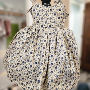 May include: A sleeveless dress with a gathered skirt and a floral print in shades of blue and cream. The dress has thin straps that tie at the shoulders.