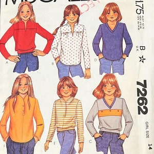 May include: A sewing pattern for girls' tops. The pattern includes five different styles: a red top, a white top with red polka dots, a blue top, a yellow top with a button-up collar, and a striped top. The pattern is for size 14.