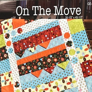 May include: A colorful quilt pattern with a variety of fabrics, including floral, polka dot, and geometric prints. The quilt is made in a patchwork style and features a variety of colors, including red, orange, yellow, green, blue, and white. The quilt is titled "On The Move" and measures 35-1/2 inches by 45-1/2 inches.