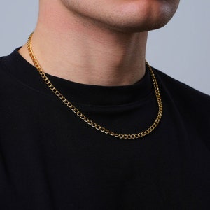 Könnte beinhalten: Eine goldene Kettenkette, die von einer Person getragen wird, die ein schwarzes Shirt trägt.