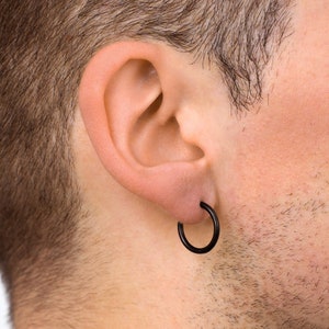 May include: A close-up of a black hoop earring in a person's ear. The earring is a simple, circular design, and the skin around the ear is visible. The person's hair and neck are also partially visible in the background.