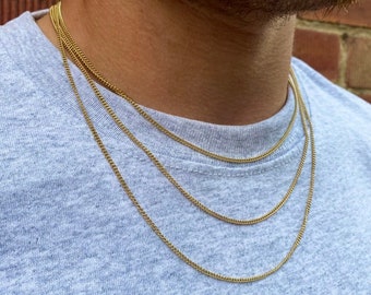 May include: A close-up of a person wearing a gray t-shirt with four gold chain necklaces layered on top of each other.