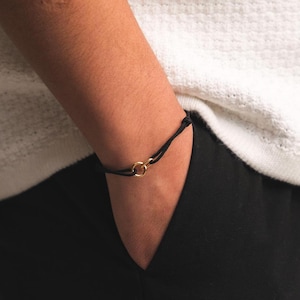 May include: A black cord bracelet with a gold double ring charm.