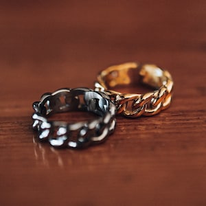 Peut inclure: Deux anneaux en chaîne, l'un argenté et l'autre doré, sur une surface en bois.