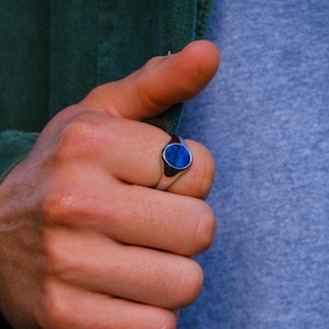 Puede incluir: Un anillo de sello de plata con una piedra ovalada azul.