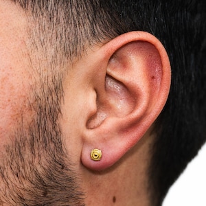 May include: A close-up of a person's ear with a small gold earring. The earring is a simple, round design with a textured surface.