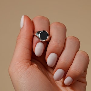 Könnte beinhalten: Ein silberner Ring mit einem schwarzen ovalen Stein. Der Ring befindet sich an einem Finger.