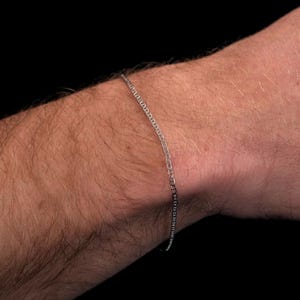 May include: A silver chain bracelet on a person's wrist.