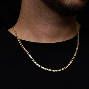 May include: A gold chain necklace with a mariner link style. The chain is worn by a person with a beard and a black shirt.