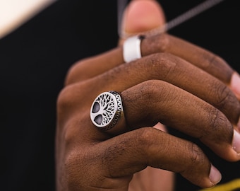 May include: A silver ring with a tree of life design. The ring is worn on the index finger of a person's hand.