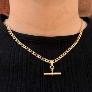 Peut inclure: Un collier en chaîne dorée avec un pendentif en forme de barre dorée. La chaîne est de style curb.
