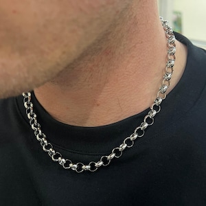 Könnte beinhalten: Eine silberne Kettenkette im Curb-Link-Stil. Die Kette besteht aus kleinen, runden Gliedern, die in einem durchgehenden Muster miteinander verbunden sind.
