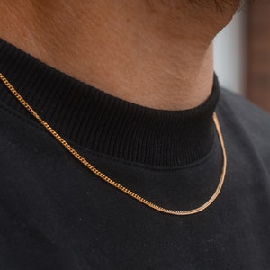 May include: A gold chain necklace worn over a black shirt.