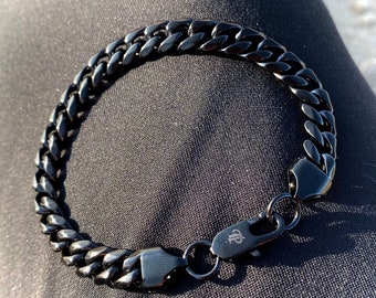 Puede incluir: Un brazalete de cadena de metal negro con cierre de broche.