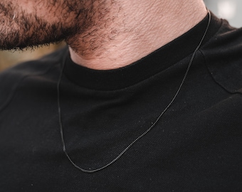 May include: A black chain necklace worn by a person with a black shirt.
