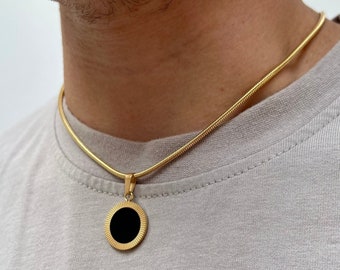 May include: A gold chain necklace with a round black pendant. The pendant has a gold rim.