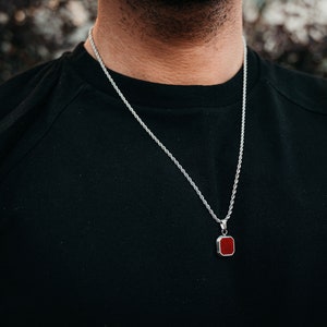 May include: A silver chain necklace with a red square pendant.
