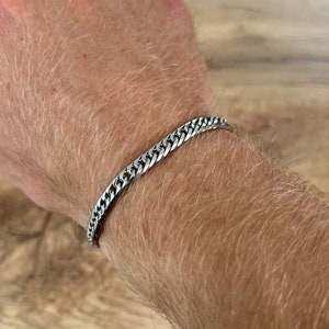 May include: A silver chain bracelet on a person's wrist.