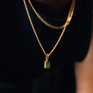 May include: A gold-toned necklace featuring a rectangular emerald green gemstone pendant suspended from a twisted rope chain. The pendant is set in a simple gold-colored metal frame, and the chain has a polished finish that reflects light.
