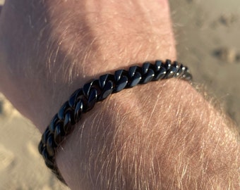 Puede incluir: Un brazalete de cadena negra con un diseño de eslabones de curb.