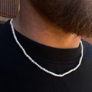 May include: A white pearl necklace on a person's neck. The necklace is made of small, round pearls that are strung together on a thin chain.
