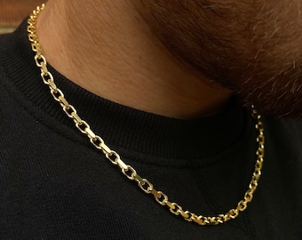 May include: A gold chain necklace with a box chain design. The chain is worn by a person with a black shirt.