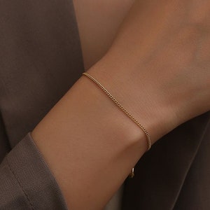Könnte beinhalten: Ein zartes goldenes Kettenarmband mit schlichtem Design.