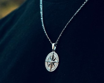 Könnte beinhalten: Eine silberne Kettenkette mit einem Kompass-Anhänger. Der Kompass ist rund und hat ein detailliertes Design.